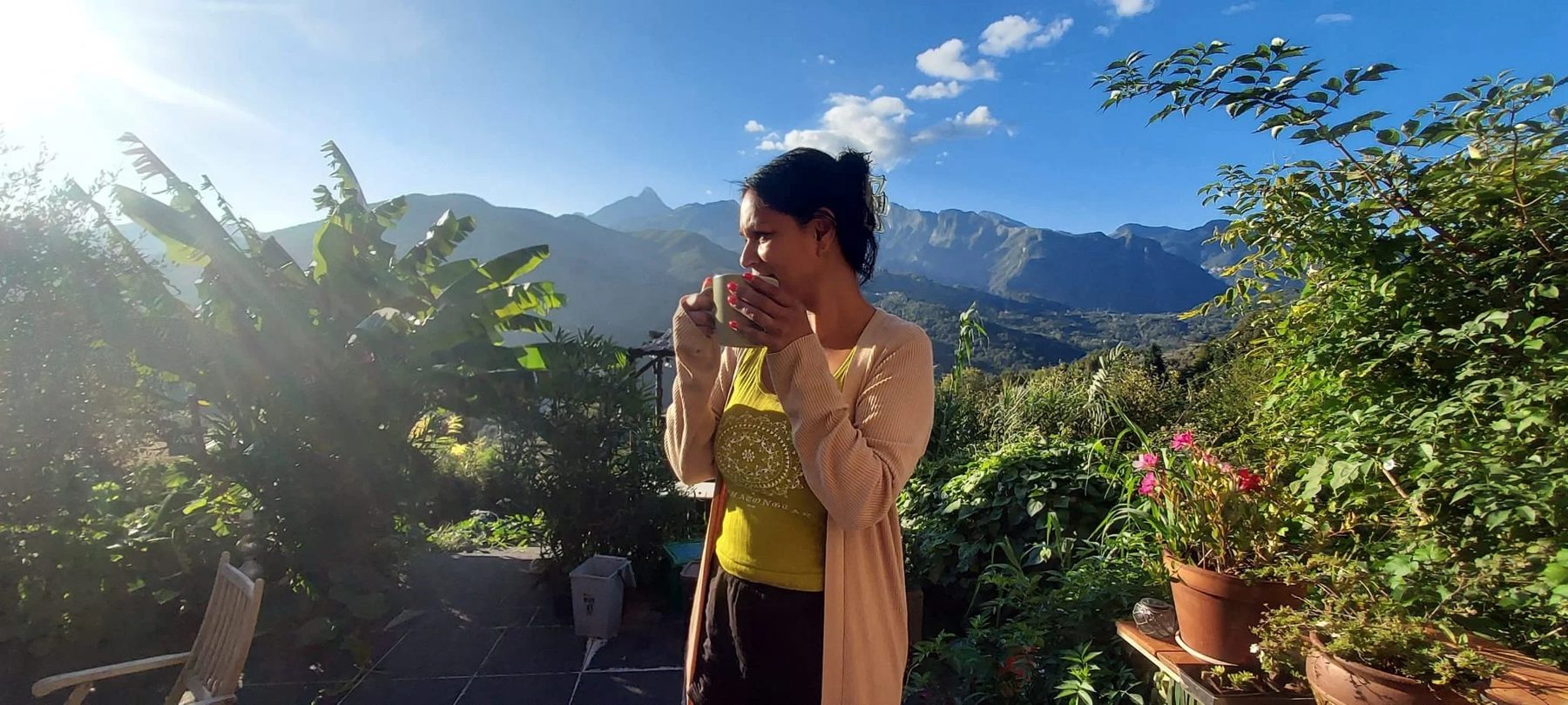 Samira with a cup of coffee, mountains behind her